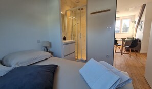 A modern bedroom with a bed, a desk, and a shower area.