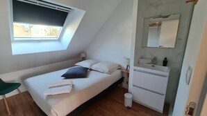 Ett litet, modernt sovrum med ett takfönster, en säng, ett sängbord med en lampa, en spegel och ett litet badrum med handfat och toalett.