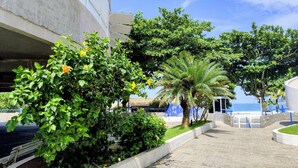 A paved pathway lined with greenery and a building with a balcony. - 12-Vista Linda Pé na Areia Guarujá-Tombo (Guarujá)