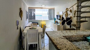 A compact kitchen with a dining area, a staircase, and a window with blinds. - 12-Vista Linda Pé na Areia Guarujá-Tombo (Guarujá)