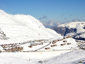 Estância de esqui no alto da montanha, coberta de neve, com vários edifícios no estilo chalé, pistas de esqui e um teleférico.