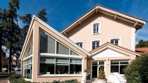 Un immeuble de deux étages avec une façade beige, de grandes fenêtres et une entrée blanche avec des marches.