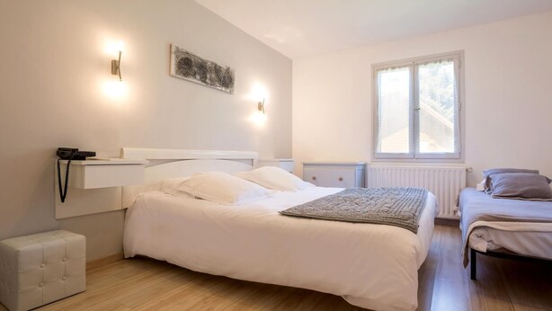 Une chambre à coucher comprenant un grand lit, un lit plus petit, une table de chevet, une commode, une lampe, un téléphone, un radiateur et une fenêtre.