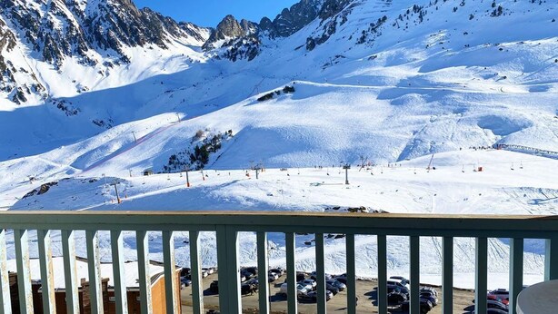 A snowy mountain landscape with a ski slope, a parking area, and a building in the foreground.