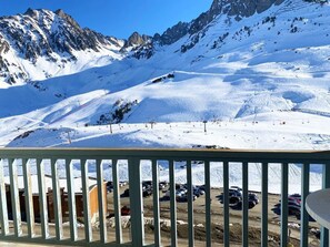 A snowy mountain landscape with a ski slope, a parking area, and a building in the foreground.