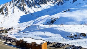 A snow-covered mountain with ski slopes, a parking area, and a building with a sign.