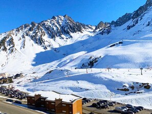 Una montaña nevada con pistas de esquí, un área de estacionamiento y un edificio con un letrero.
