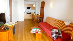 A compact living space with a kitchenette, a sofa, a dining table, and a TV.