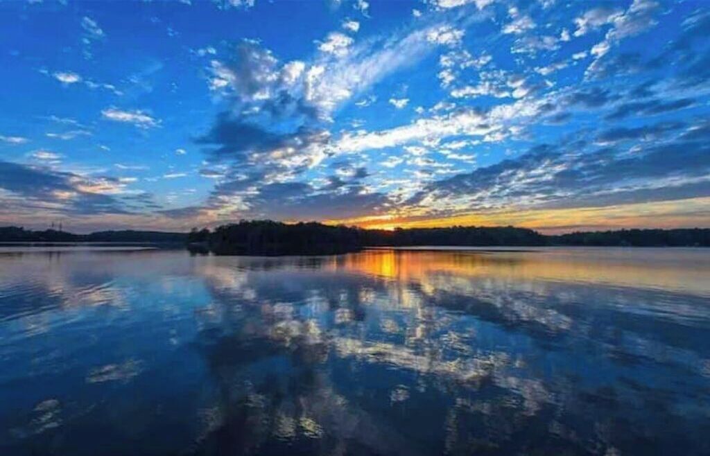 A calm lake reflecting a sunset sky with clouds.