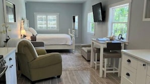 Una habitación de hotel compacta con cama, escritorio, silla, televisor y kitchenette.
