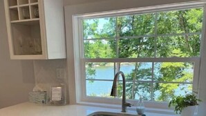 Una cocina con ventana, armarios blancos y un lavamanos.