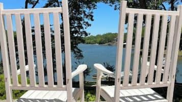 Two white Adirondack chairs facing a body of water with trees in the background.