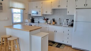 A modern kitchen with white cabinets, a central island with stools, a microwave, a stove, and a refrigerator.