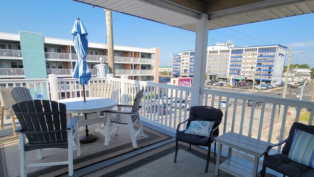 A balcony with a table and chairs, a blue umbrella, and a view of buildings and a street.