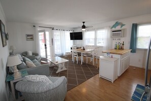 Un espace de vie compact comprenant un canapé, une table à manger, des chaises, un téléviseur et une kitchenette.
