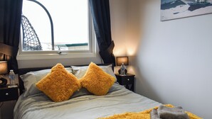 A hotel room with a bed, two pillows, a water bottle, a lamp, and a view of the outside.
