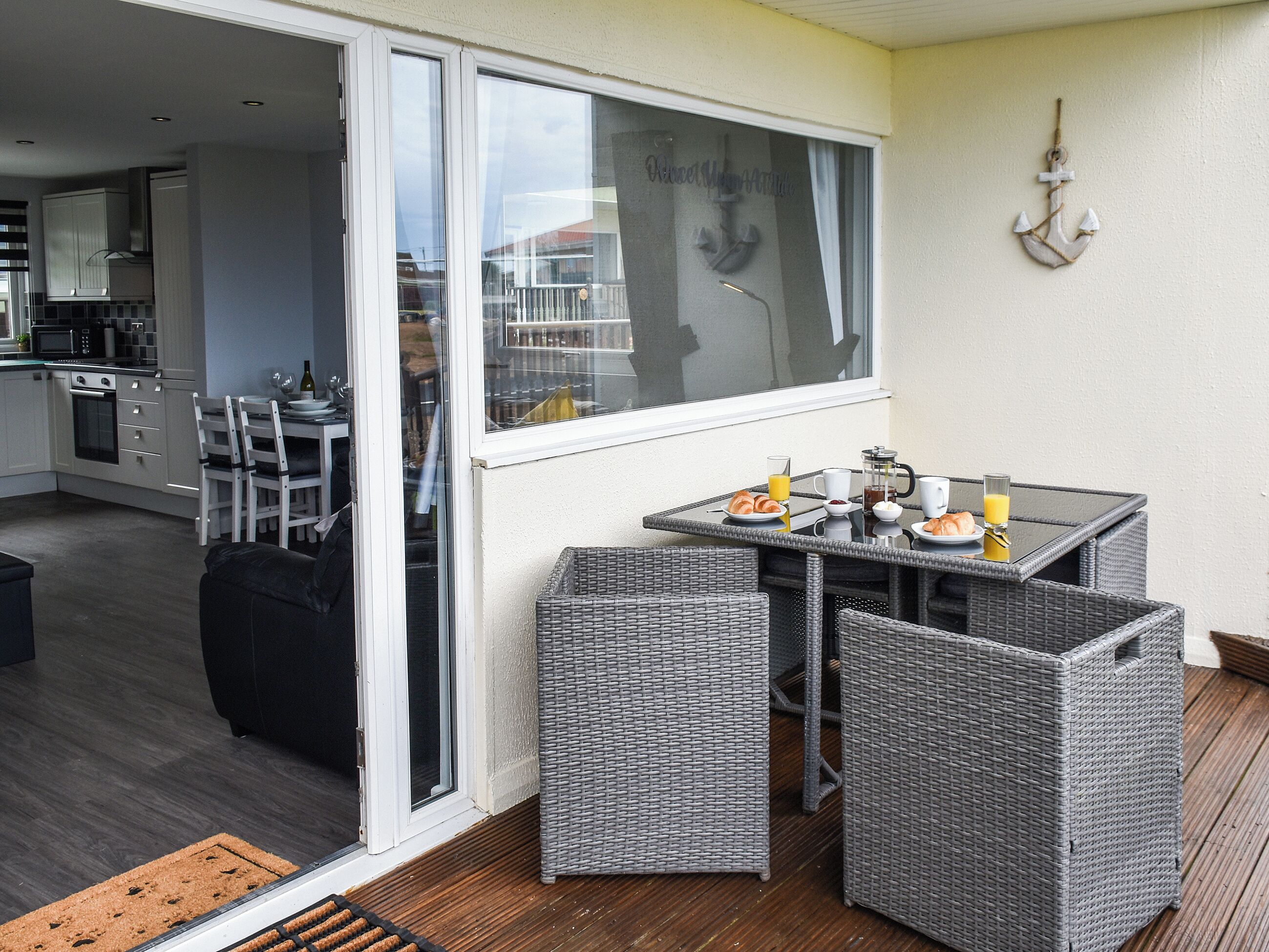A balcony with wicker furniture, a breakfast setup, and a view of the kitchen.