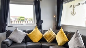A black leather sectional sofa with four pillows in various colors and a decorative anchor on the wall.