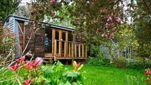 Une cabane en bois dotée d’un balcon, entourée d’une végétation luxuriante et de plantes en fleurs.