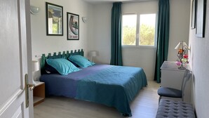 Ein Schlafzimmer mit Bett, Nachttisch, Lampe und einem Fenster mit Vorhängen.