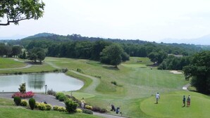 Ein Golfplatz mit Teich, Bäumen und einer hügeligen Landschaft im Hintergrund.