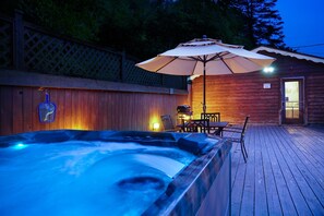 A wooden deck with a hot tub, an umbrella, and a small building with a door. - Riverside Suite*HotTub*WiFi*Steps to the River (Elkins)