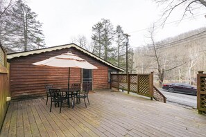 A wooden deck with a table and chairs, a covered patio area, and a view of a road and trees.