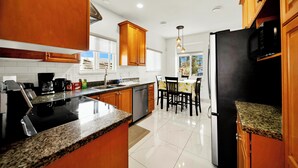 A kitchen with granite countertops, wooden cabinets, a stainless steel refrigerator, and a dining area with a table and chairs. - Newly Renovated Home Heart of Vancouver Near YVR, Skytrain, Downtown (AC) (Vancouver)
