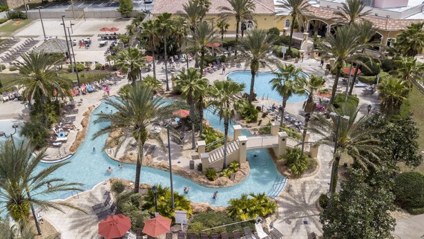 Un resort con piscina central, palmeras y un edificio de techo con tejas.