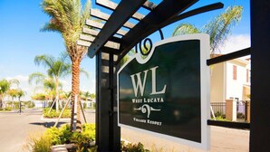 A sign for West Lucaya Village Resort with a palm tree and a clear sky in the background.