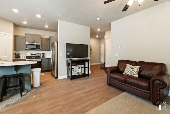 Relax in this stylish living space with a kitchen and seating area, featuring a flat-screen TV, microwave, stove, and refrigerator.