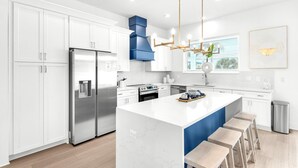 A modern kitchen with white cabinetry, stainless steel appliances, and a central island with bar stools. - Nautilus! Sleeps 22! Ocean View! Rooftop Deck (Destin)