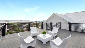 A rooftop terrace with white furniture, a small table with a plant, and a view of the ocean and buildings. - Nautilus! Sleeps 22! Ocean View! Rooftop Deck (Destin)