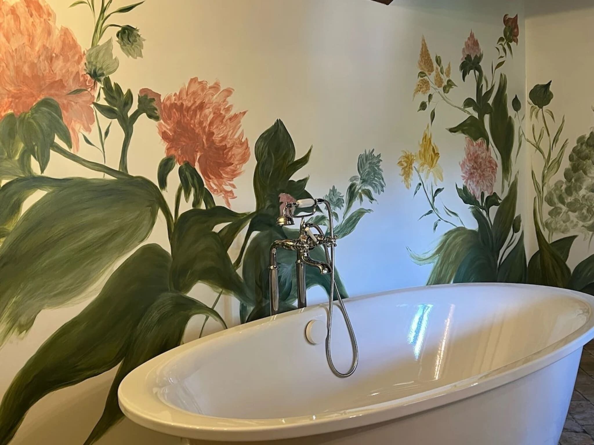 A bathtub with a faucet, surrounded by a floral mural.