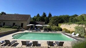 A swimming pool with lounge chairs and umbrellas, surrounded by a stone wall and greenery.