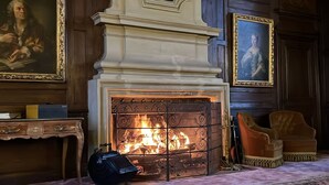 A room with a fireplace, wooden paneling, and two framed portraits on the walls.