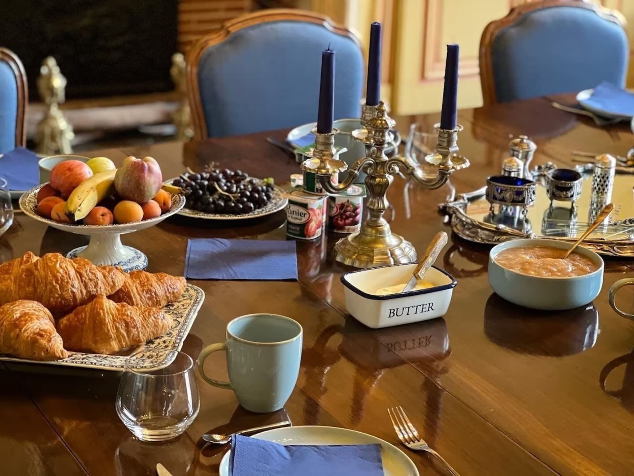 Frühstückstisch mit Croissants, Früchten und einer Butterdose auf einer Holztischplatte.