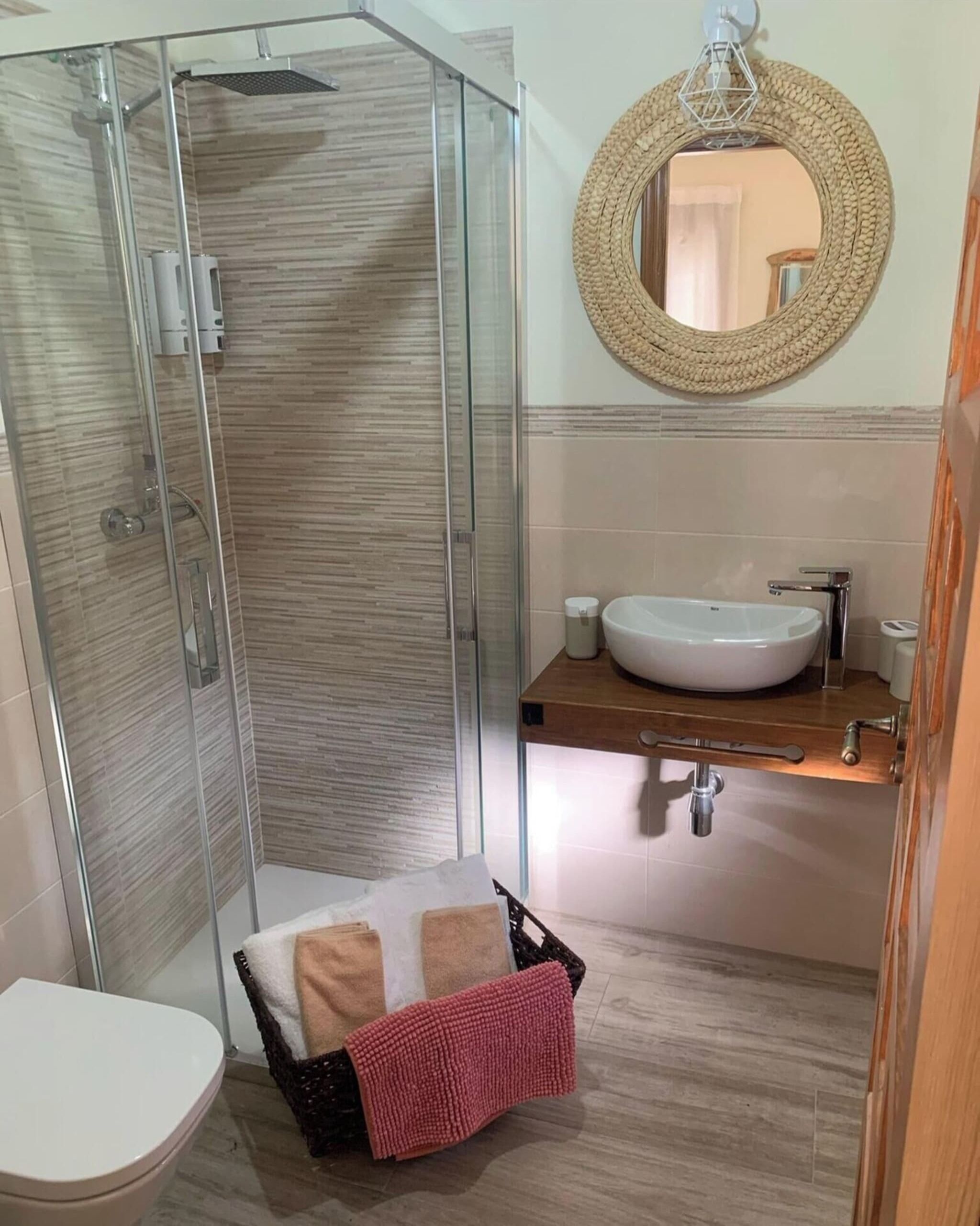 Un baño con ducha envuelta en vidrio, un lavabo blanco y un espejo redondo.