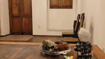 Um quarto com porta de madeira, uma janela com persianas de madeira, uma mesa de jantar com um recipiente de petiscos e uma guitarra encostada na parede.