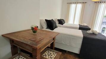 A small, cozy room with a wooden table and benches, a bed with a white and black bedspread, and a hanging light fixture.