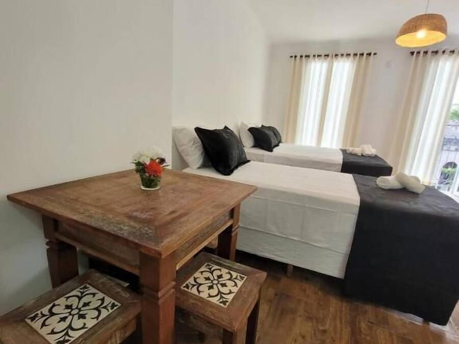 A small, cozy room with a wooden table and benches, a bed with a white and black bedspread, and a hanging light fixture.