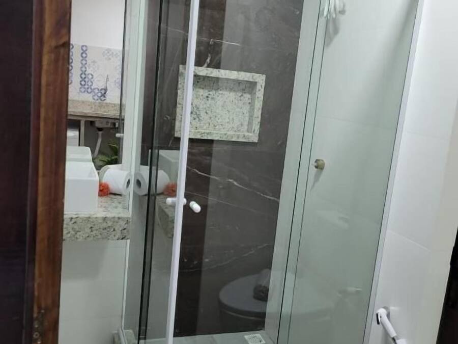 Cabina de bany amb envàs de vidre, porta blanca, taulell de marbre i una petita estantella.