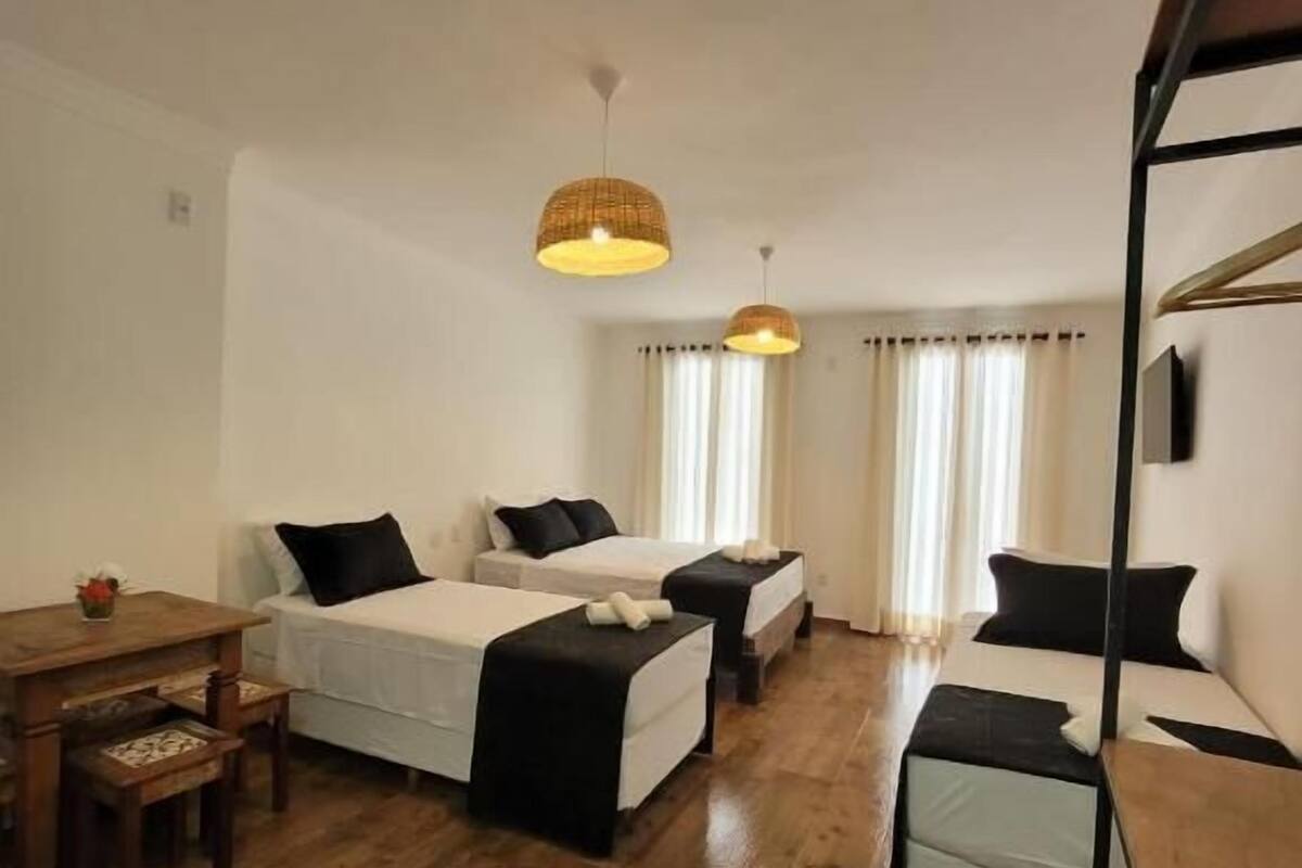 A room with two beds, a wooden table, and two hanging lamps.