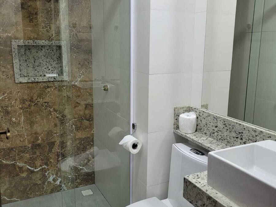 A bathroom with a glass-enclosed shower, a toilet, a sink, and a marble-tiled wall.
