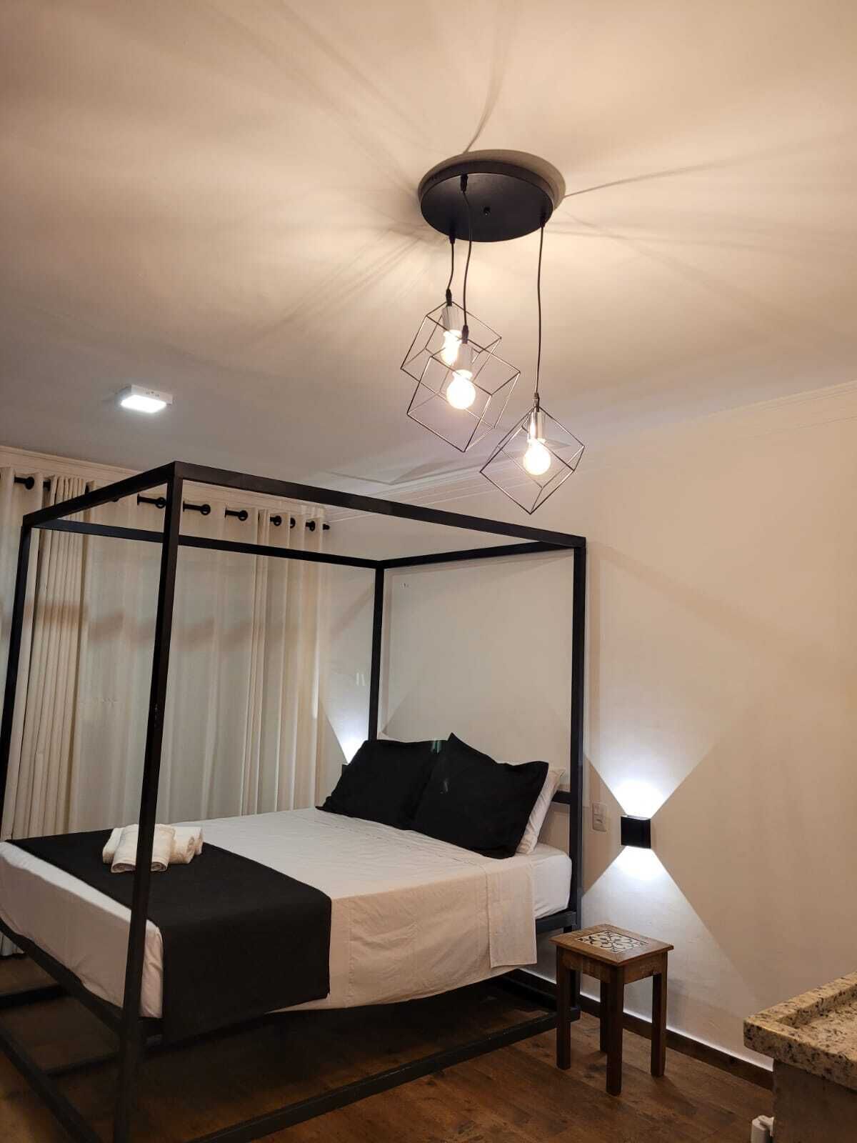 Un dormitorio moderno con una cama con dosel, una pequeña mesita de madera y una lámpara de techo original.