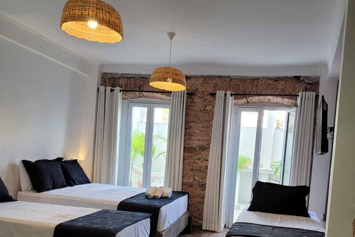 A hotel room with two beds, a wooden floor, a chair, and a large window with curtains.