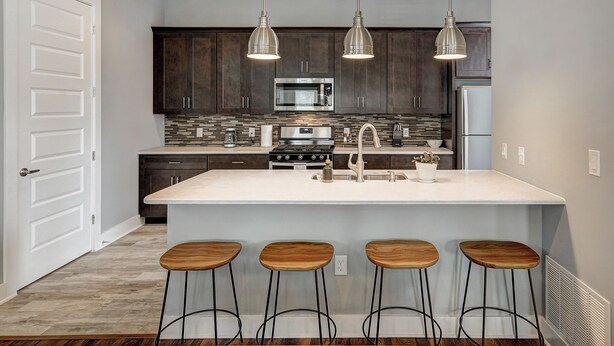 A modern kitchen with dark wood cabinets, a large island with bar stools, stainless steel appliances, and pendant lighting. - Next to Rainey St, Town Lake, Super Cozy with Modern Aesthetic (Austin)