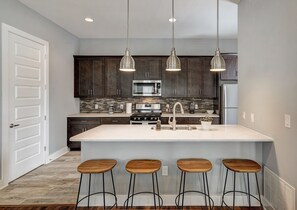 A modern kitchen with dark wood cabinets, a large island with bar stools, stainless steel appliances, and pendant lighting. - Next to Rainey St, Town Lake, Super Cozy with Modern Aesthetic (Austin)