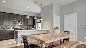 A modern kitchen with dark wood cabinets, stainless steel appliances, and a large island with a wooden table and benches. - Next to Rainey St, Town Lake, Super Cozy with Modern Aesthetic (Austin)