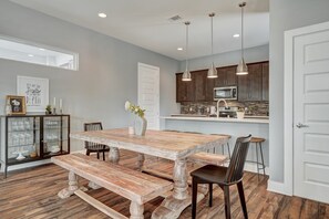 Un coin repas avec une table et des bancs en bois, un buffet avec des portes en verre, et une cuisine en arrière-plan.